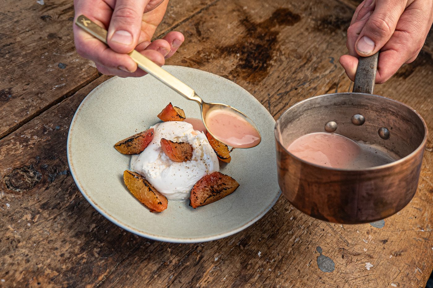 Dessertteller mit Burrata und gegrillten Pflaumen, dazu wird Sauce aus einem Kupfertopf angegossen