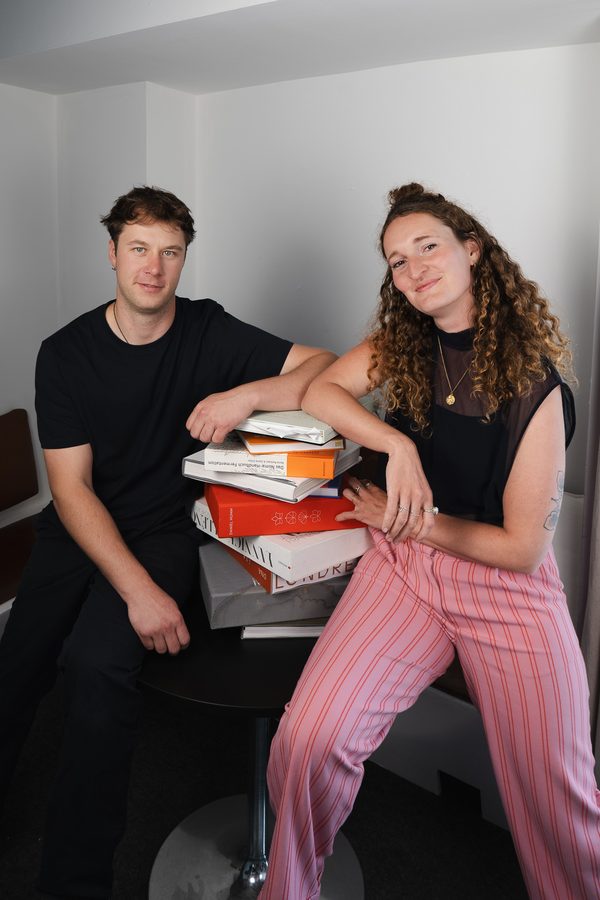 Anne und Lukas sitzen nebeneinander, zwischen ihnen ein Stapel Kochbücher